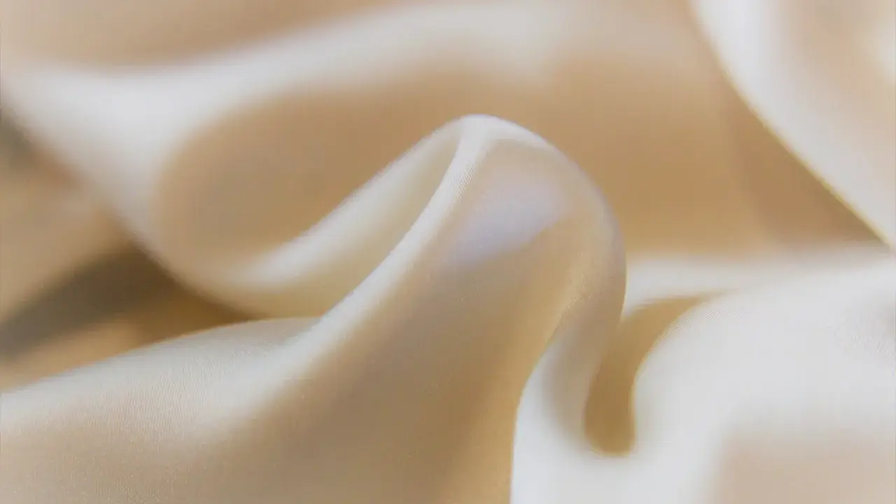 Mjuka veck av ljusbeige cupro-material som glänser.