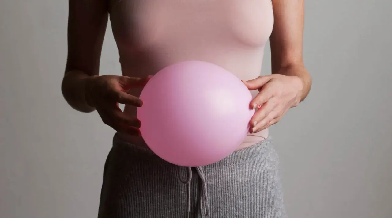 En person håller en rosa ballong mot magen, som om den vore uppsvälld och gör att personen känner sig dålig i magen.