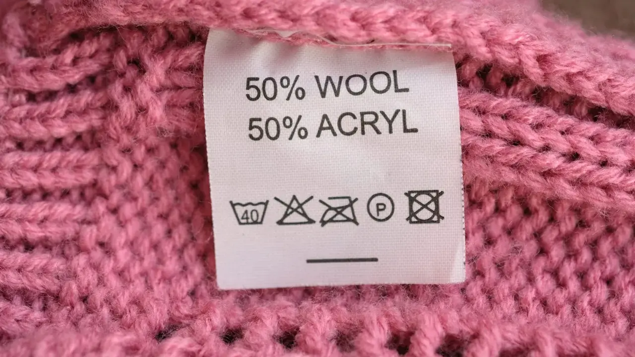 En rosa stickad tröja med en etikett som visar 50% ull och 50% akryl.