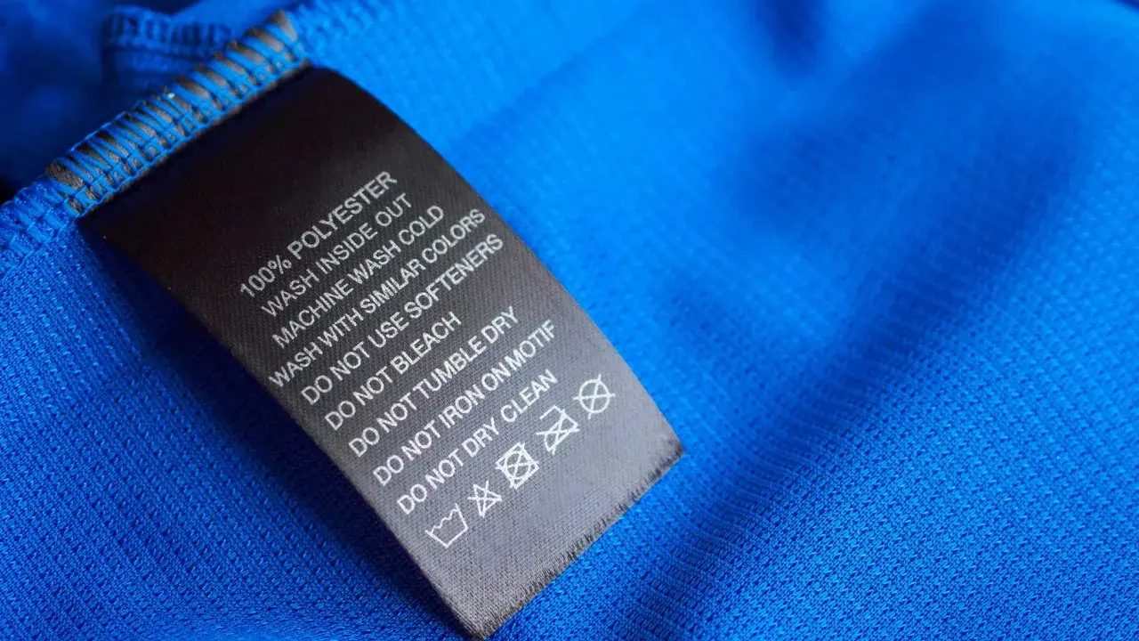 Tvättlapp på blått tyg visar 100% polyester. Skillnaden mellan polyamid vs polyester är viktig för skötselråden.