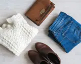 En vit kabelstickad tröja, jeans, bruna stövlar och en brun handväska. Perfekt för en kapselgarderob lista.