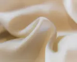 Mjuka veck av ljusbeige cupro-material som glänser.