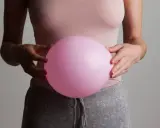 En person håller en rosa ballong mot magen, som om den vore uppsvälld och gör att personen känner sig dålig i magen.