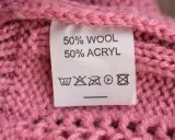 En rosa stickad tröja med en etikett som visar 50% ull och 50% akryl.