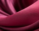 Mörkröd textil med veck och en fin ribbad textur. En visuell presentation av olika tyger.