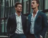 Två stiliga män i kostym framför en modern byggnad. En perfekt stilguide herr för den moderna mannen.