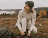Kvinna i viskos svett-underställ knyter kängor i svensk natur.