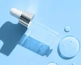 En pipett med klar vätska, som innehåller hyaluronsyra och retinol, ligger på en ljusblå bakgrund med droppar av serum.