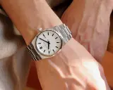 En person bär en silverfärgad klocka med vit urtavla på vänster handled. Vilken arm har man klockan på?