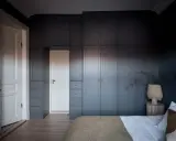 Mörka garderober i stockholm stil ramar in en vit dörr. En vas med grenar står på ett sidobord bredvid en säng.