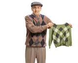 Äldre man med argyle-tröja håller upp en mindre, likadan tröja. Han ser bekymrad ut, som om bomullen krymper.