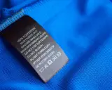 Tvättlapp på blått tyg visar 100% polyester. Skillnaden mellan polyamid vs polyester är viktig för skötselråden.