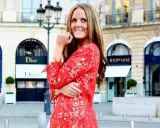 En kvinna i röd spetsklänning poserar framför Dior i Paris. Drömmer om ett jobb inom mode.