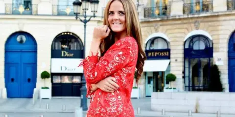 En kvinna i röd spetsklänning poserar framför Dior i Paris. Drömmer om ett jobb inom mode.