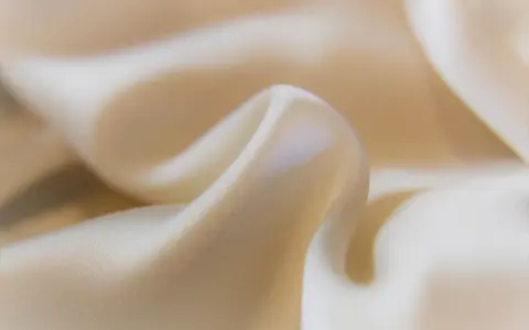Mjuka veck av ljusbeige cupro-material som glänser.
