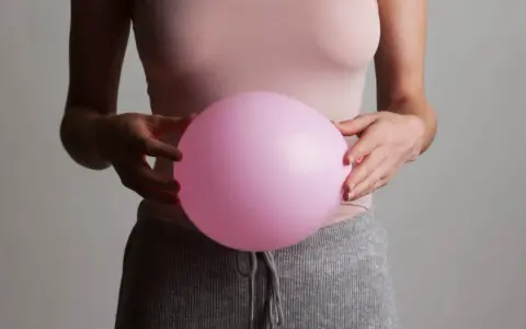 En person håller en rosa ballong mot magen, som om den vore uppsvälld och gör att personen känner sig dålig i magen.