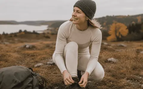 Kvinna i viskos svett-underställ knyter kängor i svensk natur.