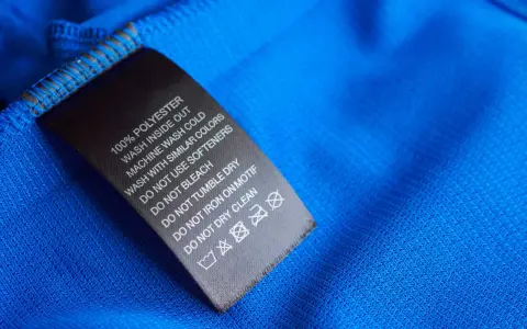 Tvättlapp på blått tyg visar 100% polyester. Skillnaden mellan polyamid vs polyester är viktig för skötselråden.