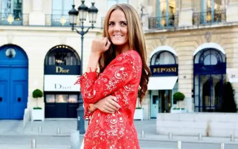 En kvinna i röd spetsklänning poserar framför Dior i Paris. Drömmer om ett jobb inom mode.