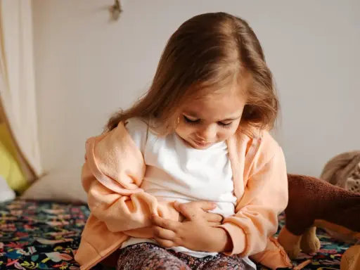 Liten flicka med magont, håller sig om magen. Hon verkar ha magsjuka symtom.