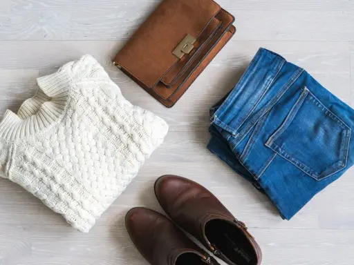 En vit kabelstickad tröja, jeans, bruna stövlar och en brun handväska. Perfekt för en kapselgarderob lista.