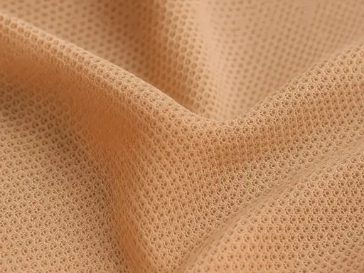 Nära bild av ett hudfärgat, nätliknande tyg. Materialet är mjukt och följsamt, perfekt för andas polyamid-kläder som ger komfort hela dagen.