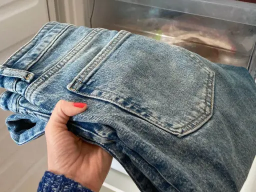 Hand håller nya jeans som luktar illa, placerade i en frys för att fräscha upp dem.