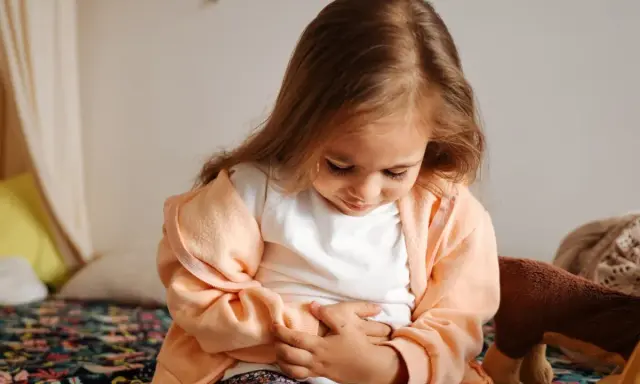 Liten flicka med magont, håller sig om magen. Hon verkar ha magsjuka symtom.