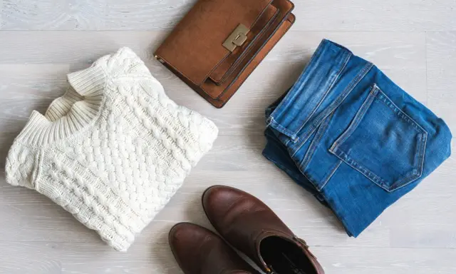En vit kabelstickad tröja, jeans, bruna stövlar och en brun handväska. Perfekt för en kapselgarderob lista.