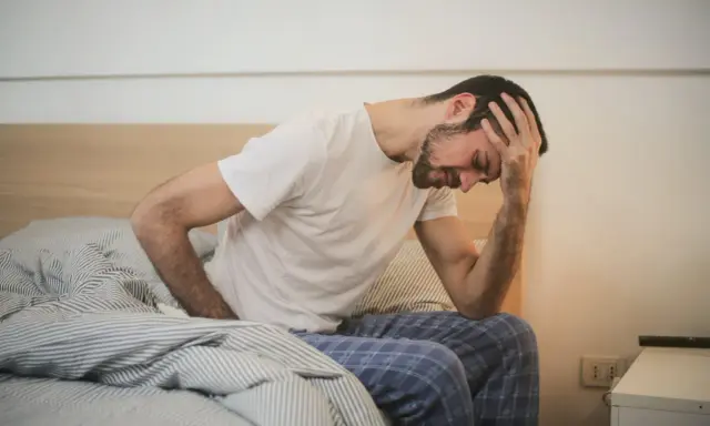 Man med handen mot pannan i sängen, ser ut att ha ont i magen. Hoppas det är något bra mot magsjuka som hjälper snart.