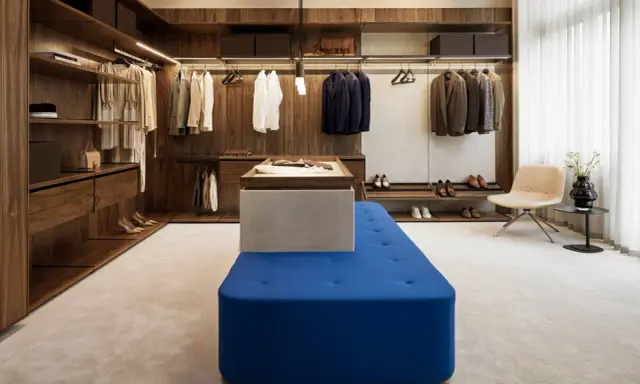 En lyxig walk-in-closet med mörka trädetaljer och en blå sittbänk, allt i en elegant italiensk stil.