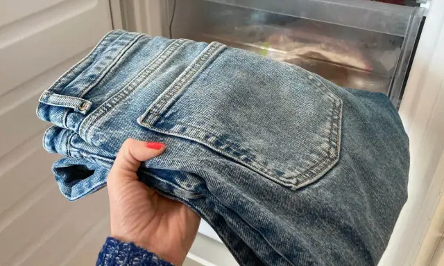 Hand håller nya jeans som luktar illa, placerade i en frys för att fräscha upp dem.