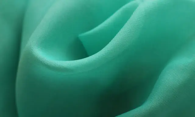 Detaljerad bild av turkos polyestertyg som visar hur tillverkas polyester genom vävning.