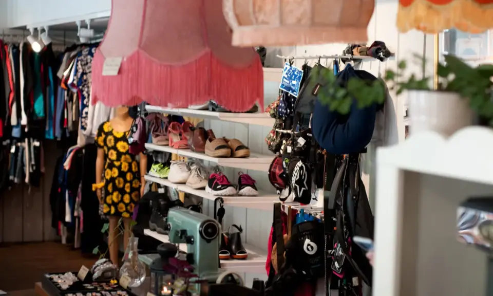 En inlämning second hand-butik med kläder på galgar, skor på hyllor och en skyltdocka i klänning.