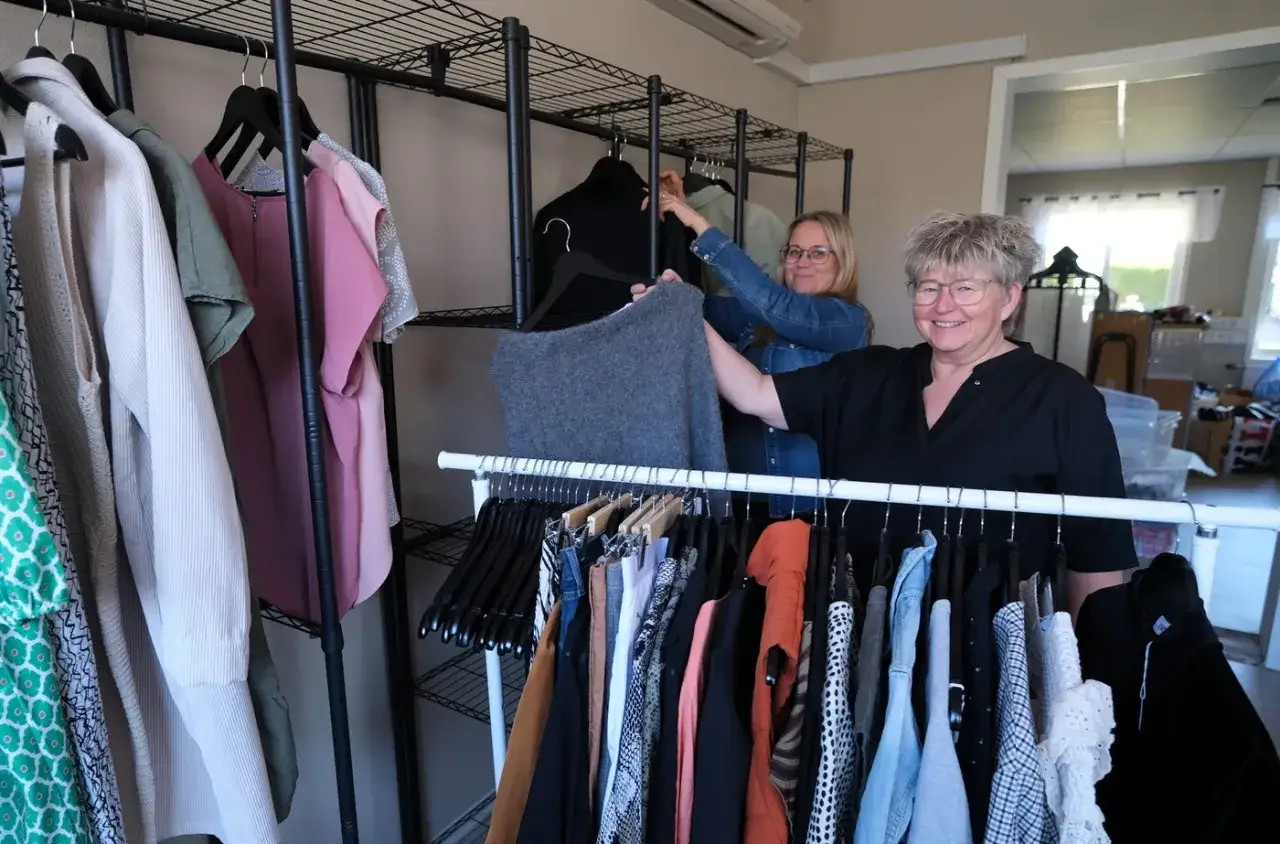 Tv&aring; kvinnor sorterar kl&auml;der p&aring; galgar i en butik f&ouml;r kommissionsf&ouml;rs&auml;ljning.