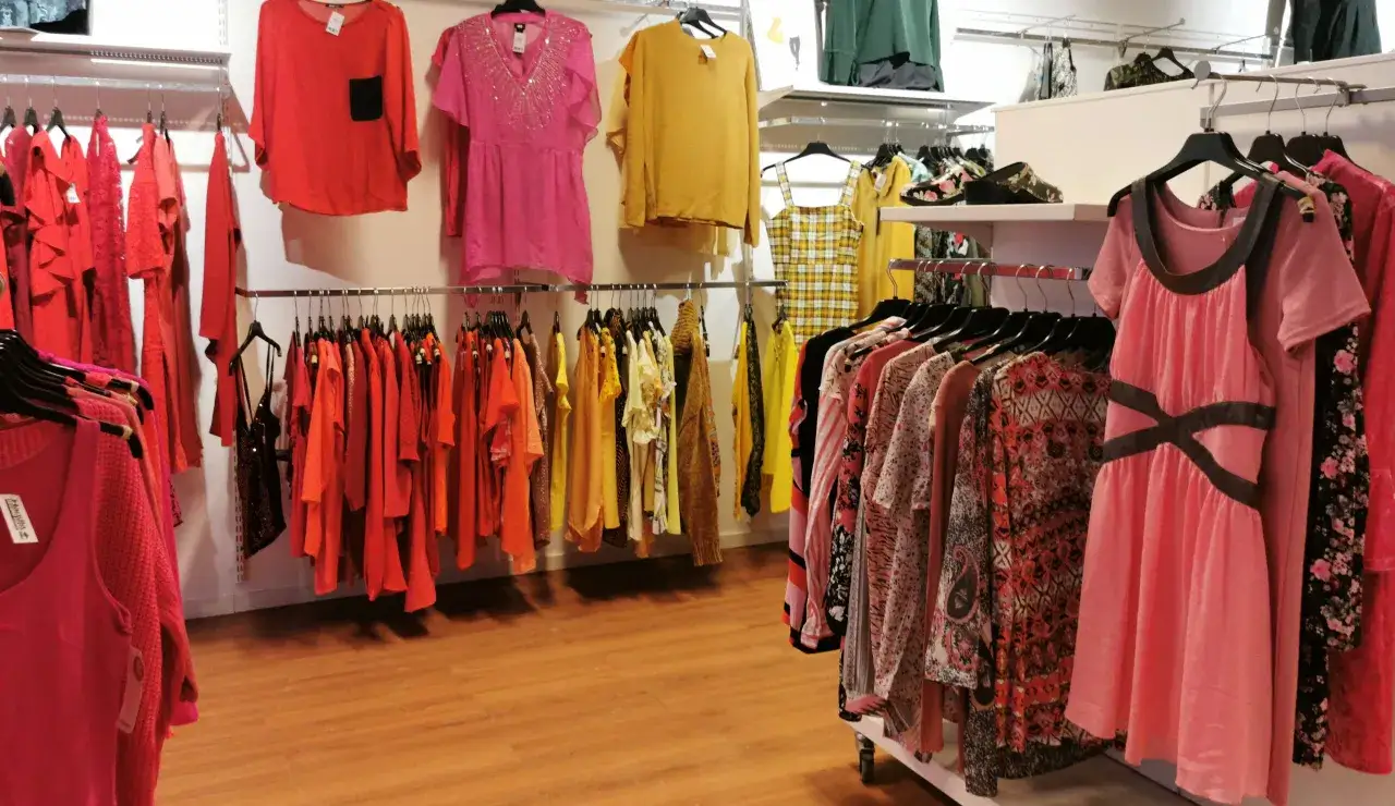 H&auml;rliga kl&auml;der i starka f&auml;rger h&auml;nger p&aring; galgar i en butik, som en stor loppis med fynd f&ouml;r alla.
