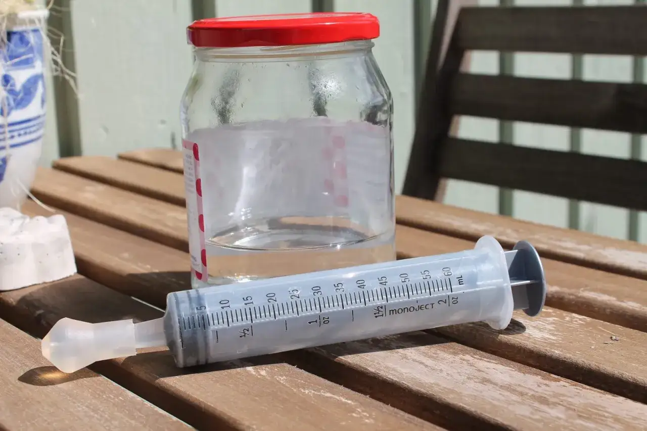 Glasburk med vatten och en stor spruta, redo för en huskur mot bihåleinflammation.