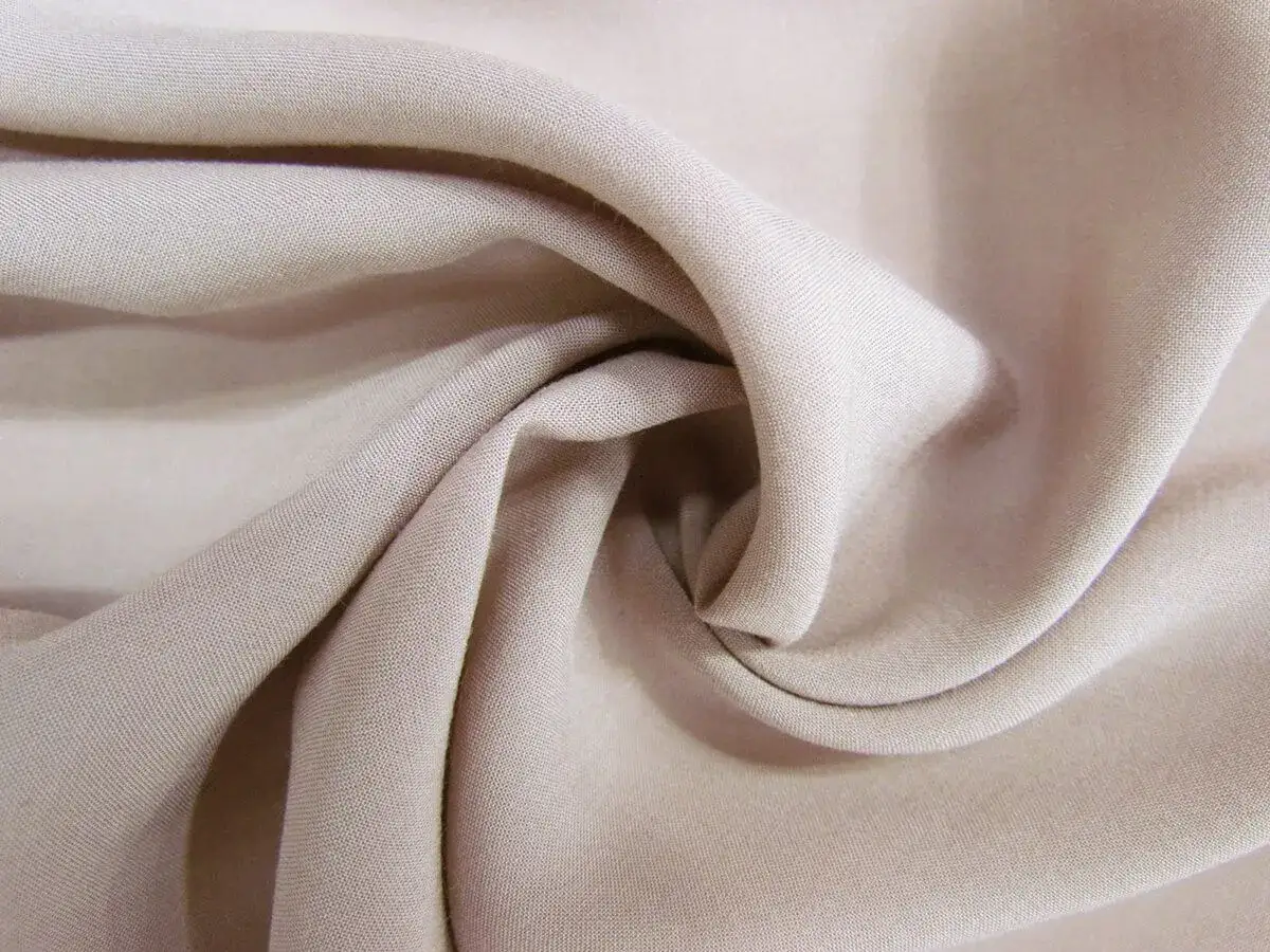 Mjukt, beige cupro material draperat i mjuka veck.